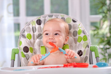 Toddler in high chair with spoon and knife