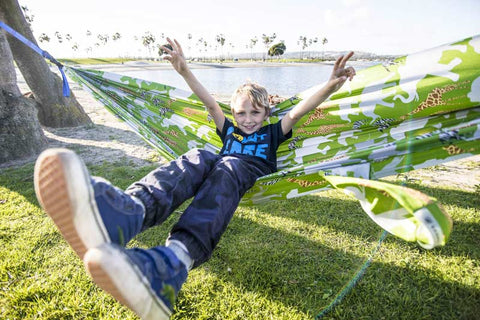 young boy in a green hammock, with his arms raised in excitement