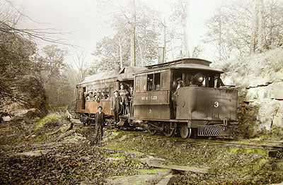Black and White image depicting a 19th century train filled with passengers and a man standing next to it, in the woods