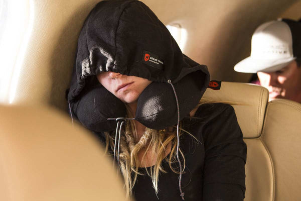 woman sleeping on a plane wearing a black hooded travel pillow