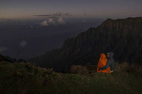 a couple sitting on a cliff edge overlooking the ocean in Kauai