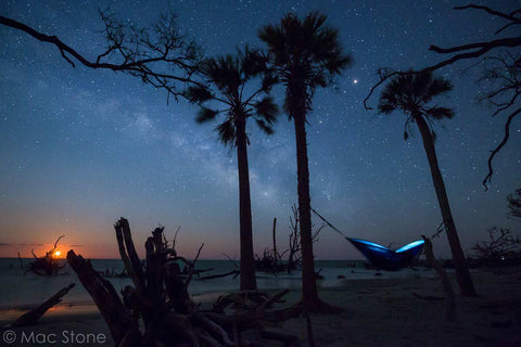 Night scene, blue hammock hung by the beach featuring a starry nighttime sky