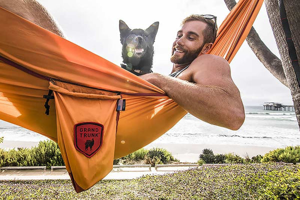 Man hammocking by the beach with his dog