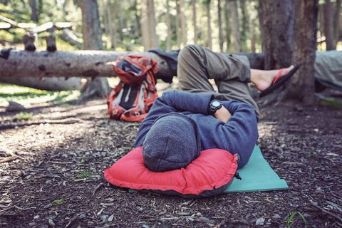 woman resting her head on a fluffy travel pillow in the woods
