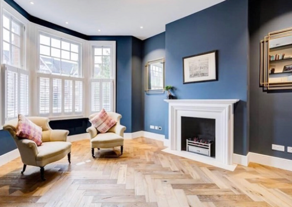 large living room with fire place, blue wall and bay window dressed with shutters