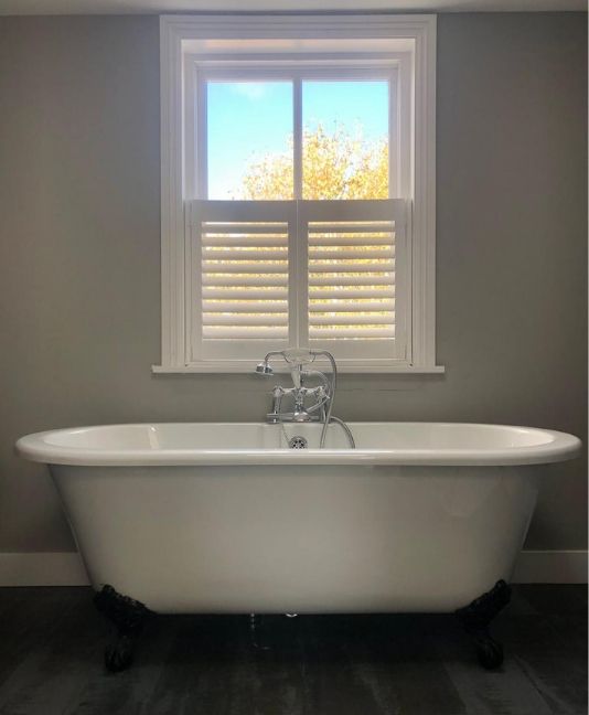 bath tub under a window with cafe style shutters