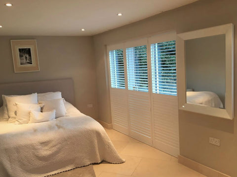 bedroom with plantation shutters on the window and lights coming through from the upper part