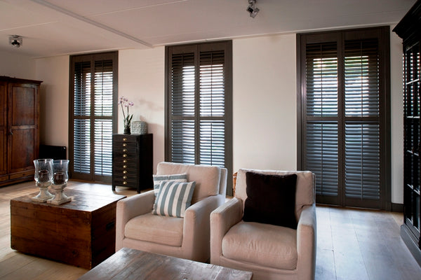 stylish lounge with elegant armchairs and dark plantation shutters on the three windows in the background