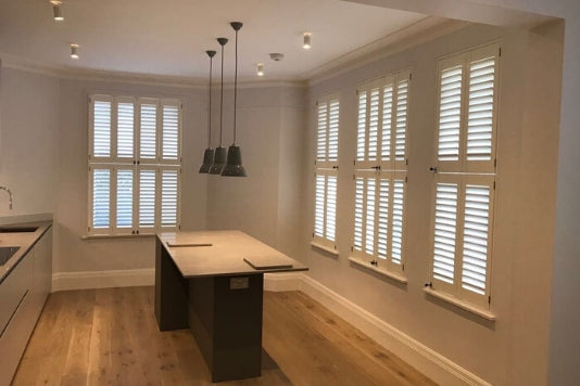 large kitchen with central wooden table and white tier on tier shutters on the window