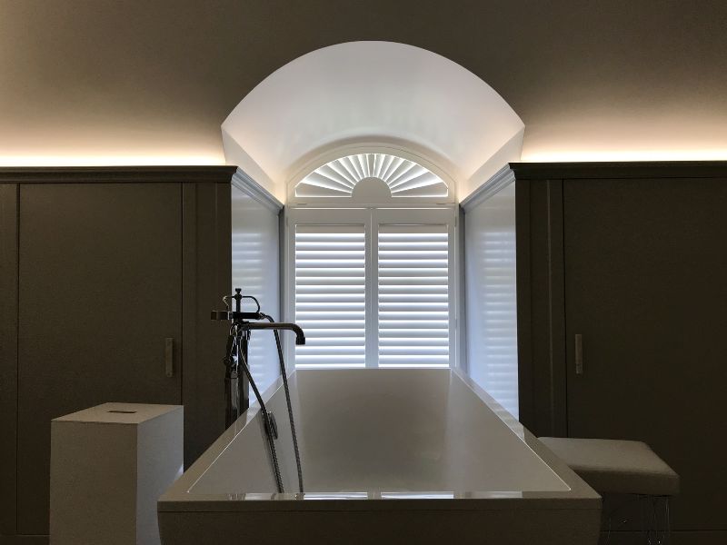 bathroom with bath tub in front of a curved window with a specially shaped shutter