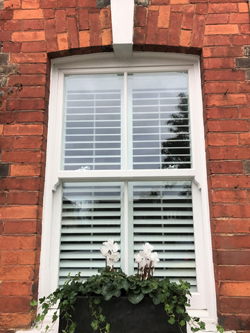 detail of the outside of a red rick house showing a sashed window with interior design shutters and flowers on the outside