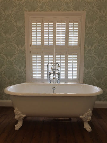 bath tub in front of a window with closed shutters