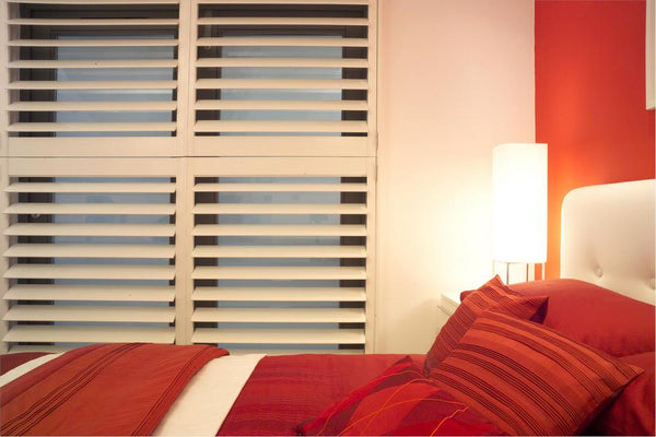 double bedroom with red covers matching the red walls and withe window shutters