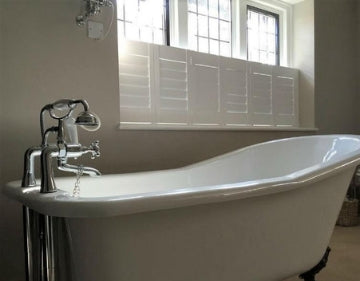 old style bath tub in a tiny bathroom white cafe style shutters on the window