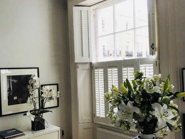 window with wooden shutters in tier on tier style, with the top open and large flower vase in front