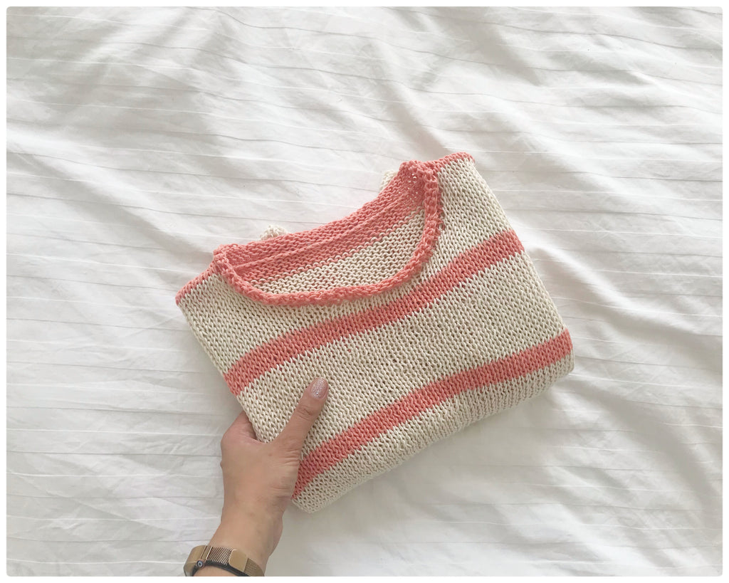 Folded Cream and Peach striped handknitted cotton tee held by hand