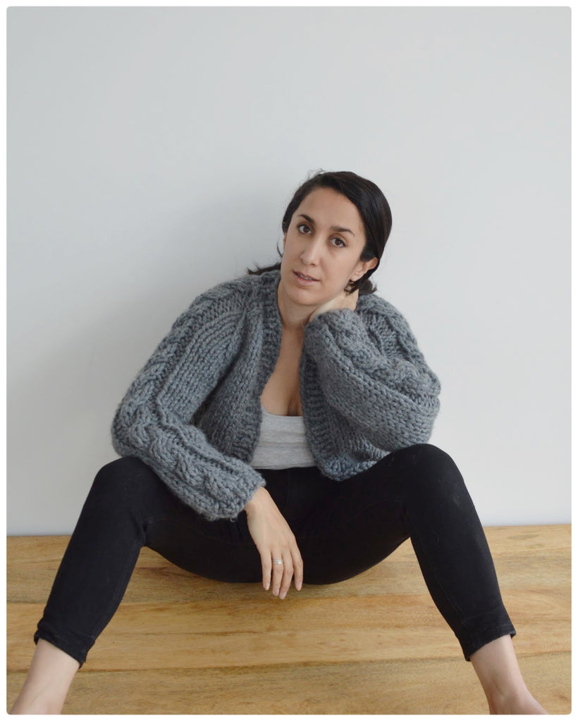 Woman sits on floor wearing grey cardigan and black jeans