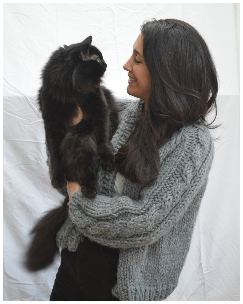 Woman with brown hair in grey cable sleeve cardigan holds black fluffy cat
