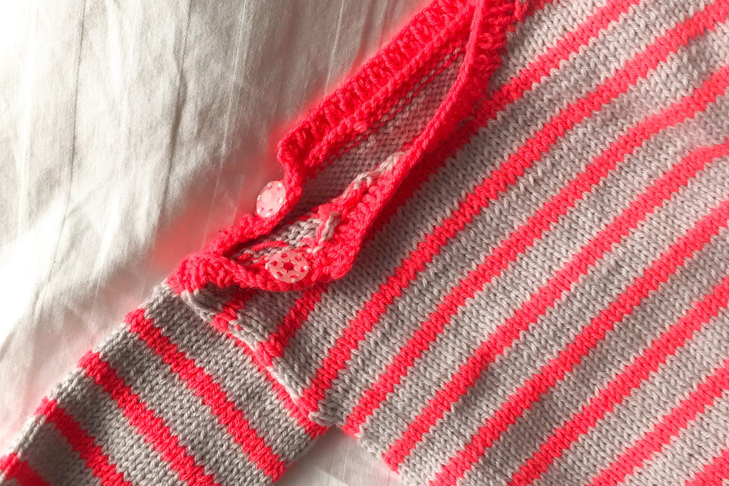 neck closure of handknitted striped baby jumper in grey and neon coral