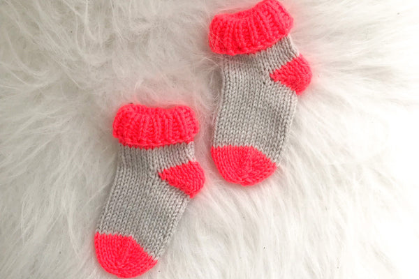 Pair of newborn socks in neon coral and grey on white background