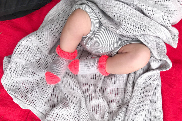 Baby’s legs wearing neon coral and grey socks on a grey cotton blanket
