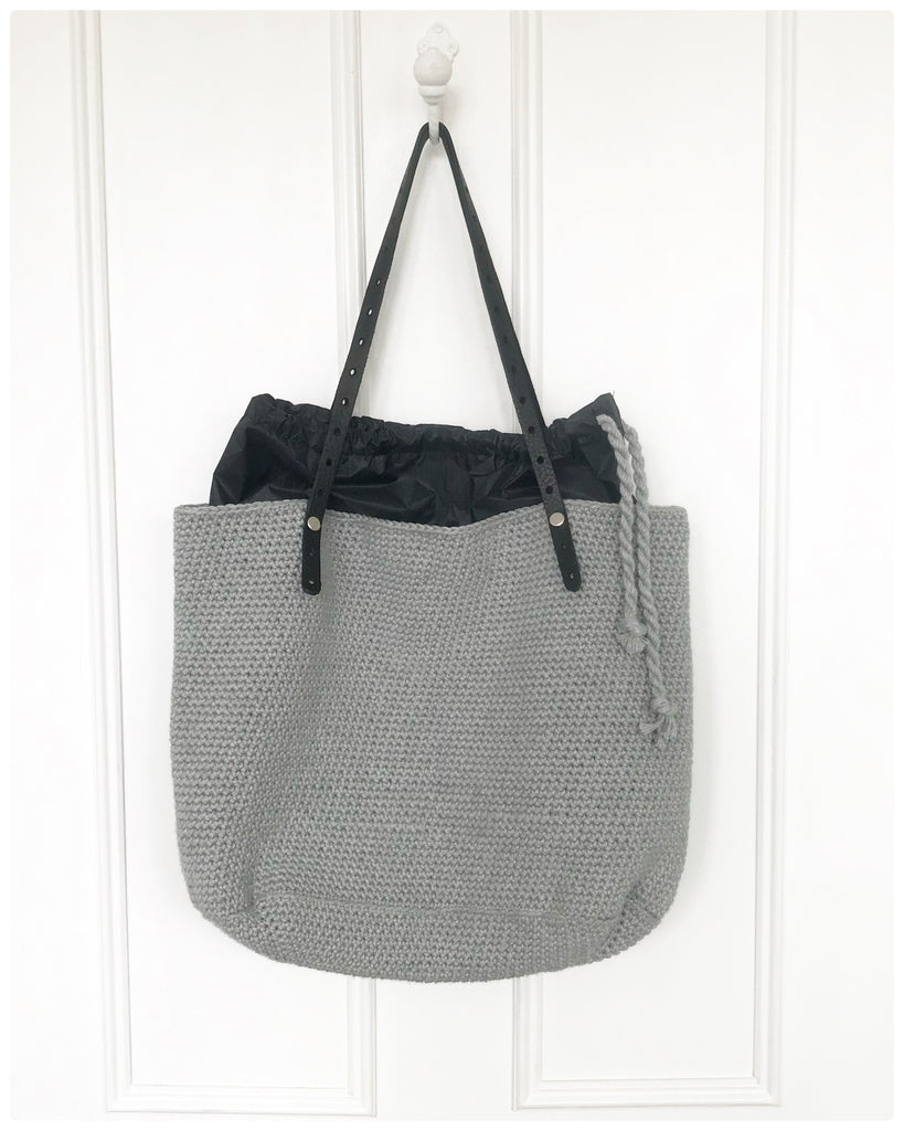 Crochet Baby-thing Bag finished, hanging on white door