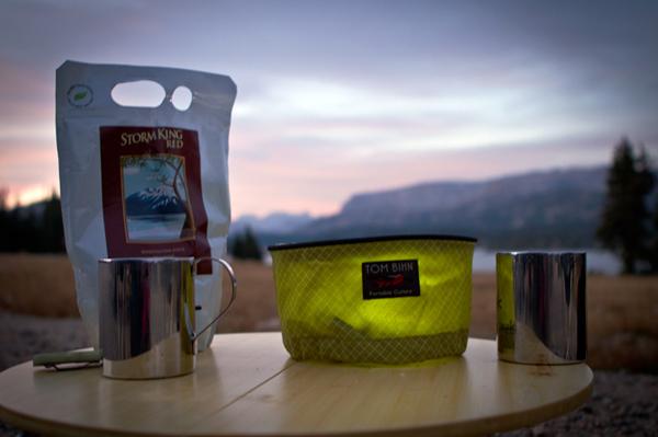 Wasabi Travel Tray, a bag of red wine, and camp mugs with a sunset in the background.
