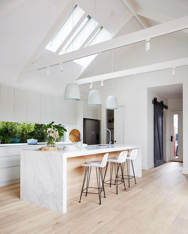 White modern kitchen with marble benchtop, 3 pandant lights and 3 rattan barstools