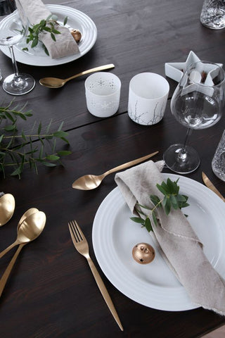 Place setting on a dark brown wooden table with star tealight holder, wine glass and rose gold cutleries