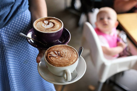Waitress holding two cups of coffee with baby in the background