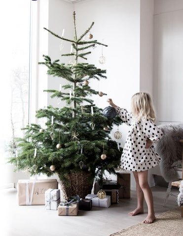 White interior with girl hanging an ornament on a sparse christmas tree