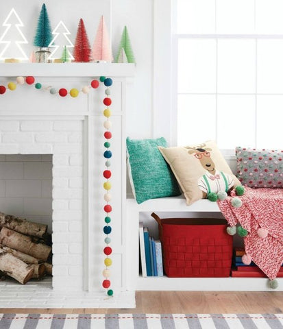 White fireplace decorated with light up trees, mini bottle brush trees and colorful felt ball garland