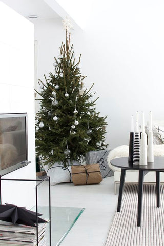 White living room with sparse Christmas tree beside a fireplace, 4 bottles on coffee table and white sofa