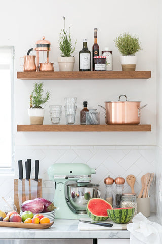 Timber floating shelves on a white kitchen wall with a variety of practical and aesthetically pleasing items including pot-plants and matching copper kitchen items.