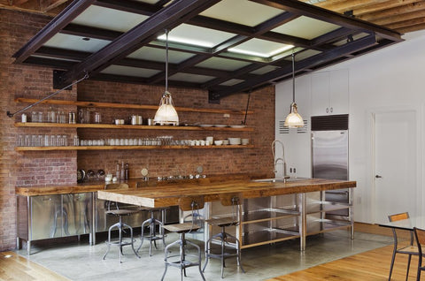Industrial kitchen interior with brick wall, long wooden shelves, stainless steel fridge and a long wooden table