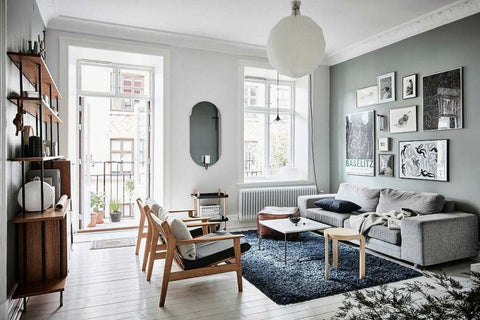 Scandinavian apartment living room interior with greyish green walls, black carpet, wooden armchairs, grey sofa, oval mirror and a round white light