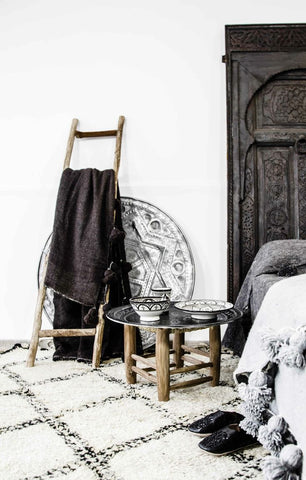 Tribal bedroom decor with black bed head, check rug, brown towel, black bedroom slippers and decorative bowls on side table