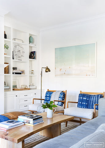 White living room interior with blue cushions, light bluish grey sofa, white cabinets and wooden coffee table