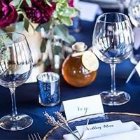 A formal table setting on blue tableclothe with a Chico Honey party favor jar