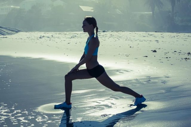 A woman is doing a lunge on the beach.