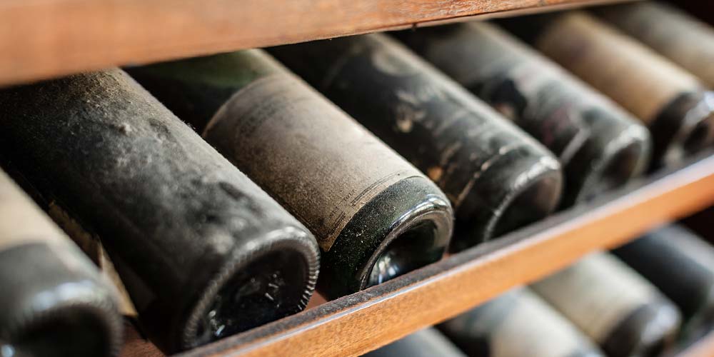 A wine cellar with aging wines gathering dust on a rack.