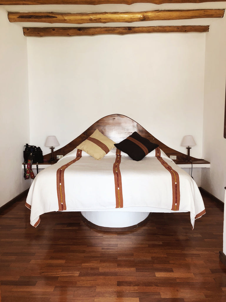 Room at tzampoc resort with wood floors and large curved wood headboard with white bedspread, Hiptipico ethical travel programs, best places to stay on Lake Atitlan, Lake Atitlan travel, ethical travel bloggers, travel ethically in Guatemala