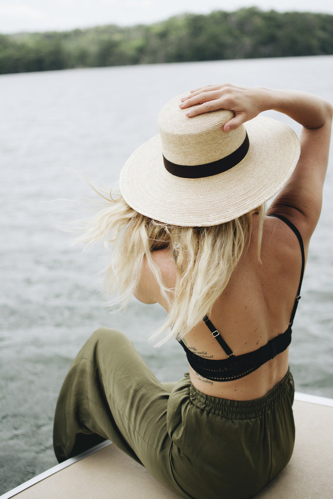 A girl with blonde hair in a wide brim Panama hat sitting on a curb