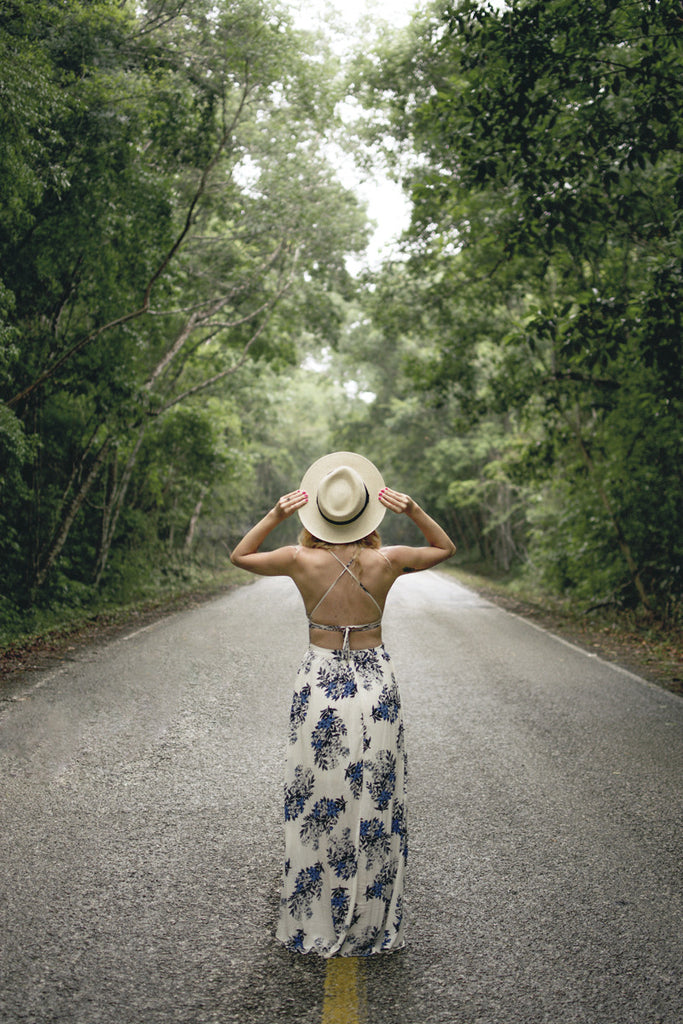 Alyssa standing in the middle of a large road in the forest wearing a long white and blue maxi dress