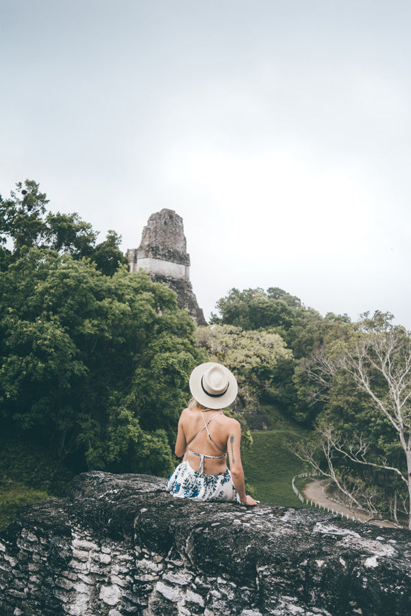 Hiptipico founder Alyssa sits on a grey stone wall looking into the distance at a Maya pyramid in Tikal, ethical travel options in Guatemala, how to get to Tikal, Tikal travel tips, what to do in Guatemala, must see destinations in Guatemala