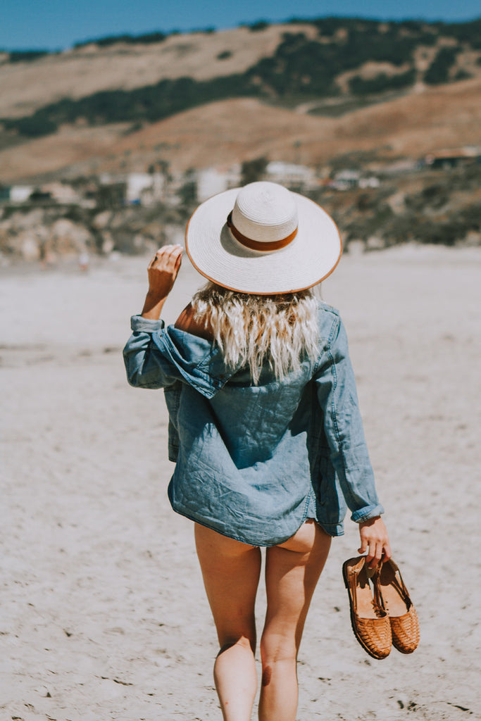 Alyssa walking down the beach as she wears a palm-tree patterned bikini and a Hiptipico wide brim hat