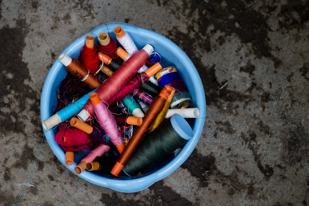 A bucket filled with vibrant various colors of thread prepared to embroider on Hiptipico fashion products, ethical fashion brands that ship to the US, ethically sourced textiles, authentic maya weaving workshop, handcrafted textile goods from Guatemala