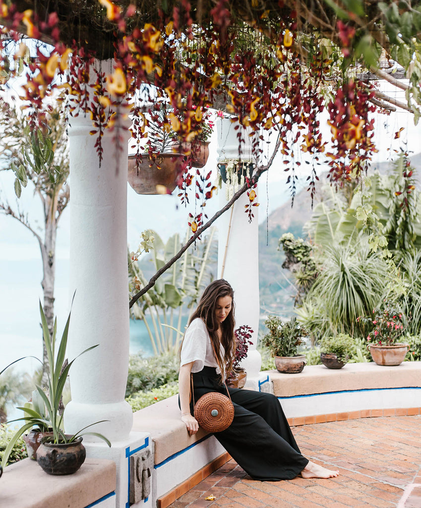 She Is Not Lost Blogger Carina Otero sits thoughtfully with Hiptipico Crossbody Bag at lookout under expanse of red and yellow hanging flowers, ethical travel bloggers, best resorts in Guatemala, where should I stay in Guatemala