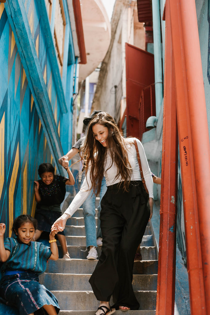 Carina Otero and Alyssa Yamamoto with local children in colorful stairway in Santa Catarina Palopó, travel bloggers, social impact bloggers, ethical travel blogs, top blogs about ethical travel, ethical travel in Guatemala, ethically travel to Lake Atitlan region