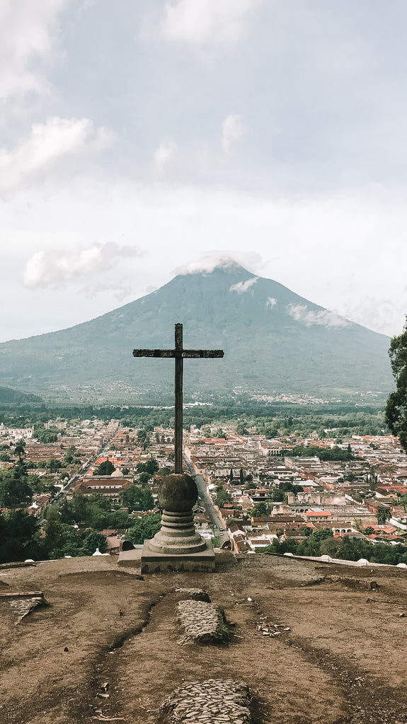 A colonial structure's cross at Cerro De La Cruz with colonial cityscape of Antigua and Volcan De Agua spanning out behind, best views in Antigua, best views Guatemala, must visit, coolest spots in Antigua Guatemala, cityscape views of Antigua, ethical travel blogs about Central America, ethical travel blogs about Guatemala, ethical travel bloggers